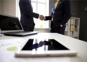 Close-shot of a tablet computer with businessmen handshaking on background