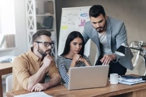 Group of confident business people in smart casual wear looking at the laptop together