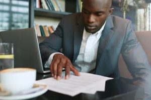 Businessman in a coffee shop reading a contract document. African business executive sitting at cafe working.